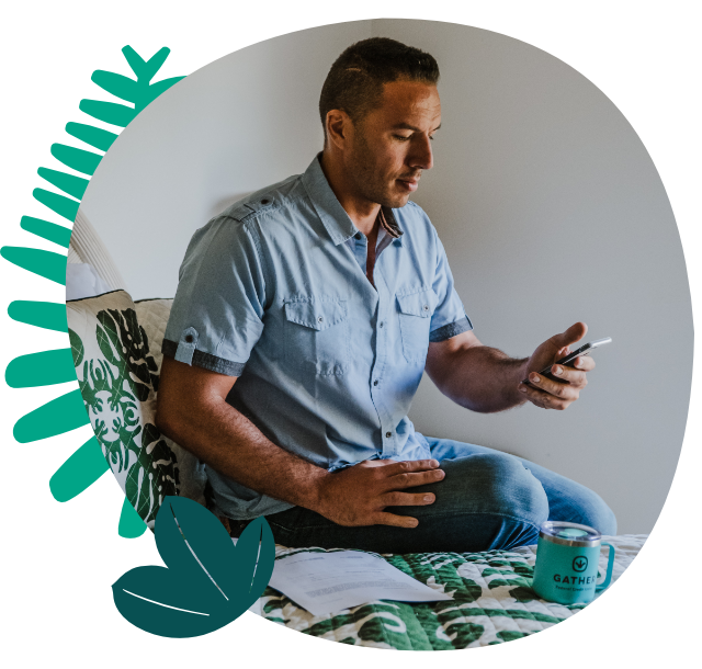 Man sitting on bed next to documents while looking at finances on mobile device